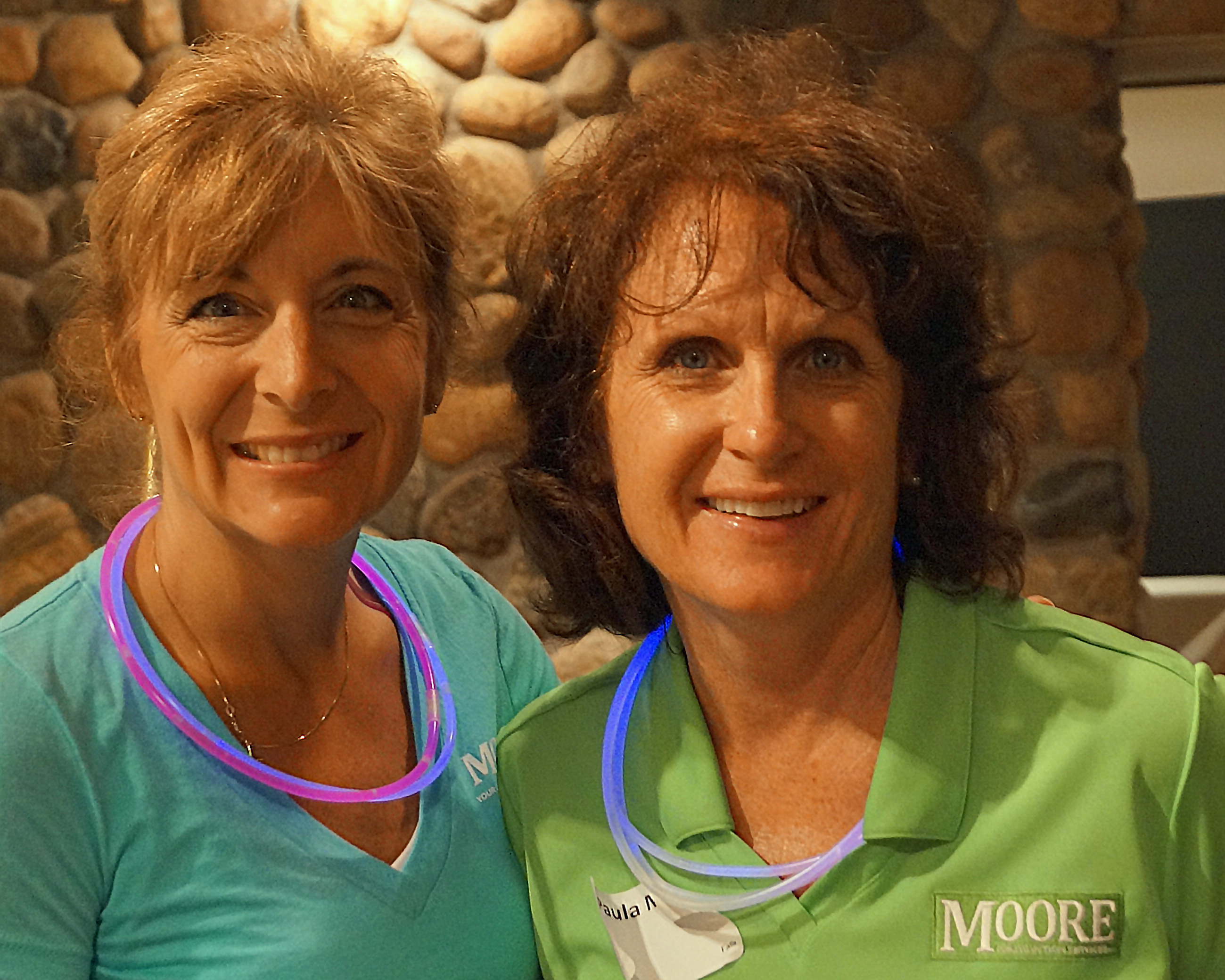 Two women are smiling brightly and wearing glow in the dark necklaces.